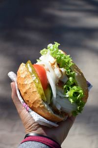 Cropped hand holding burger in sunny day