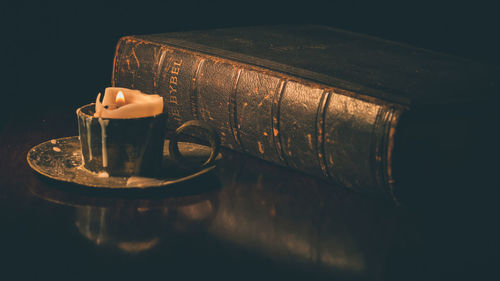 Close-up of lit candle and bible in darkroom