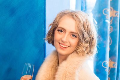Portrait of smiling woman having drink against blue wall