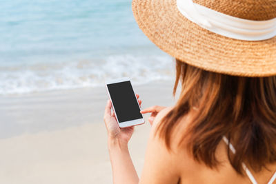Rear view of woman using mobile phone at beach