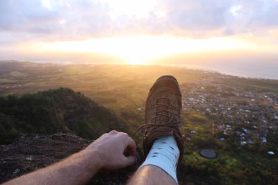 Low section of man on landscape against sunset sky