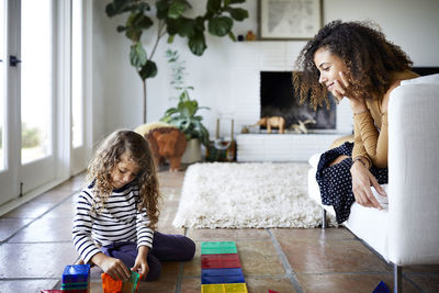 Mother looking at daughter playing with toy blocks in living room