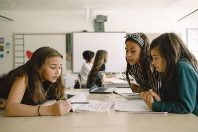 Female students studying from book while sitting by table in classroom