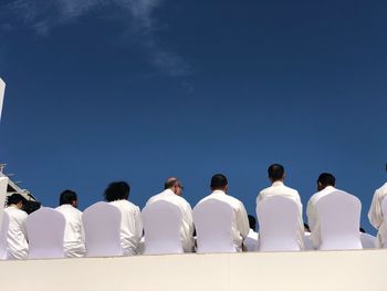 Rear view of people walking in row against clear blue sky