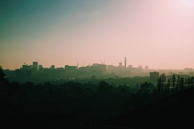 Silhouette trees and buildings against sky during sunset