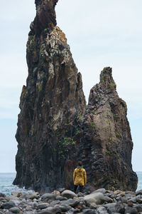 Rear view of woman standing on rocks by sea against sky