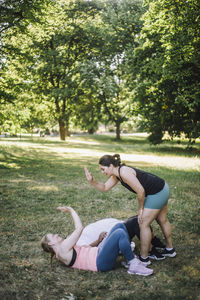 Side view of female coach giving high-five to woman lying on grass at park