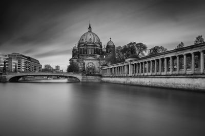 Facade of historic building by calm canal against cloudy sky