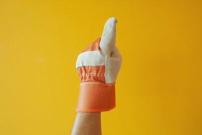 Close-up of hand wearing gloves gesturing against yellow background