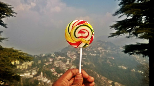 Cropped hand holding lollipop against mountain