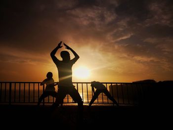 Silhouette people standing by railing against sky during sunset