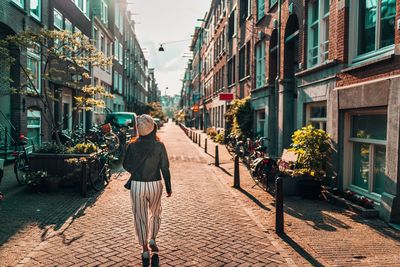 Rear view of woman walking on footpath amidst buildings