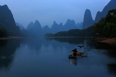 Rear view of silhouette people sailing on lake against sky