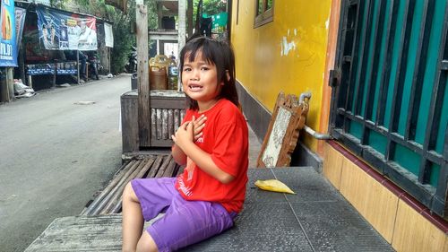 Portrait of happy girl sitting on street in city