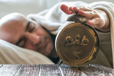 Man touching alarm clock while sleeping on bed at home