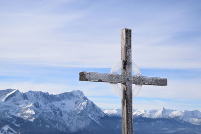 Cross on snow covered mountain against sky