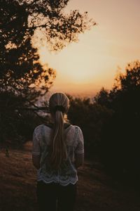 Rear view of woman standing on field against sky during sunset