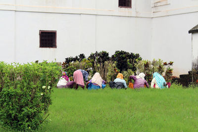 People relaxing on field against building