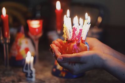 Close-up of hands holding lit candles on small cake 