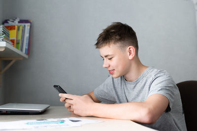 Teenage boy using smartphone for study or communication, smiling and looking at screen