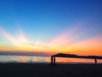 Silhouette people at beach against sky during sunset