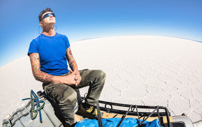 Man sitting on off-road vehicle against clear blue sky at salar de uyuni