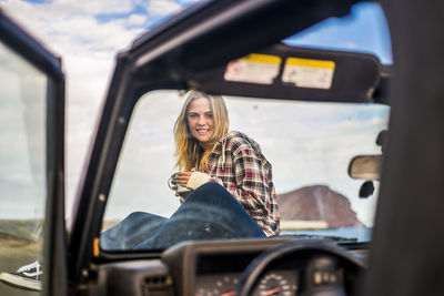 Portrait of young woman sitting by car