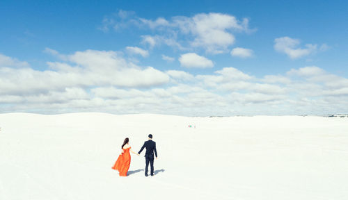 Couple walking on snowy landscape against sky