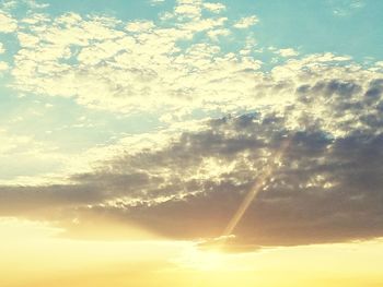 Low angle view of sunlight streaming through clouds during sunset