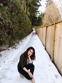 Portrait of young woman crouching on snow covered road