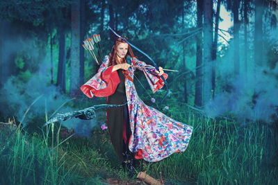 Young woman hunting with archery bow in forest 