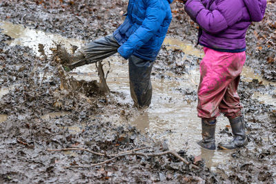 Low section of friends splashing dirty water in muddy puddle