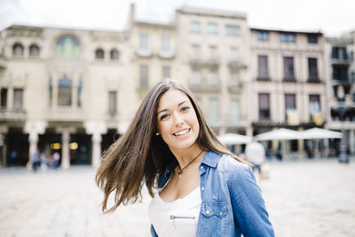 Close-up portrait of young woman against buildings in city