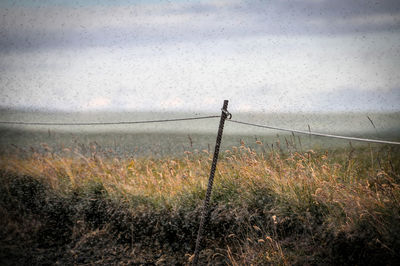 Fence on field against sky during rainy season