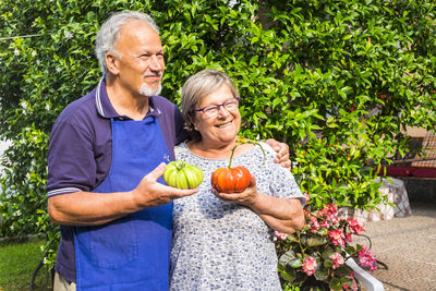 Smiling senior couple holding tomato while standing in garden at yard