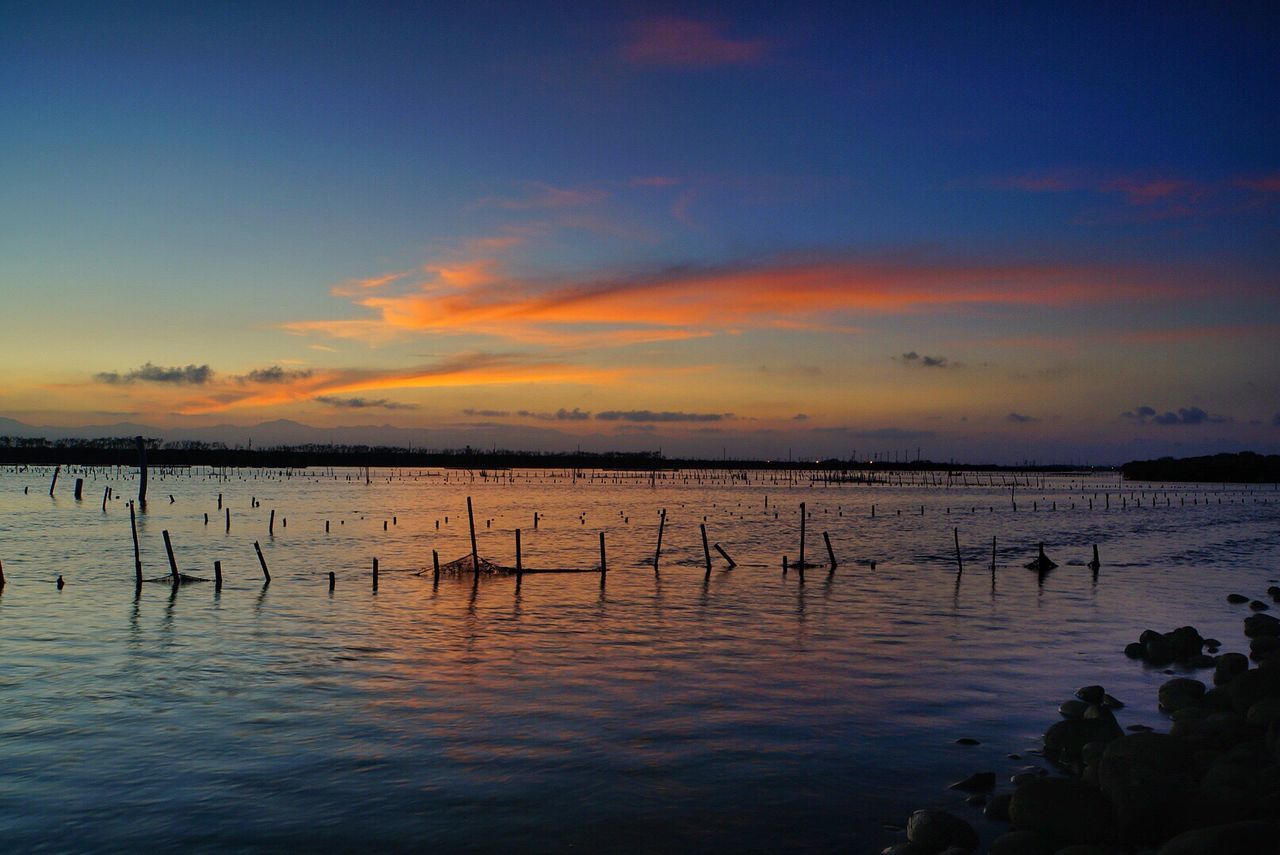 water, sunset, tranquil scene, tranquility, scenics, sky, beauty in nature, reflection, nature, idyllic, wooden post, orange color, cloud - sky, cloud, outdoors, non-urban scene, remote, no people, calm, rippled, non urban scene, ocean, blue, landscape, standing water, majestic