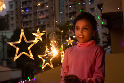 Portrait of woman holding illuminated string lights at night