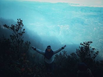 High angle view of man with arms outstretched standing against sea