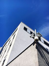Low angle view of security camera on building against blue sky