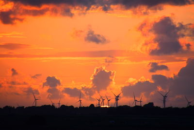 Silhouette wind turbines on land against sky during sunset