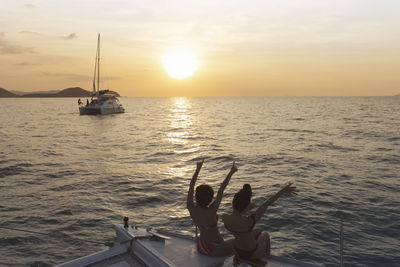 Women enjoying while sitting in boat on sea against sky during sunset