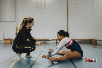 Happy teenage girl exercising while female coach guiding her in gym