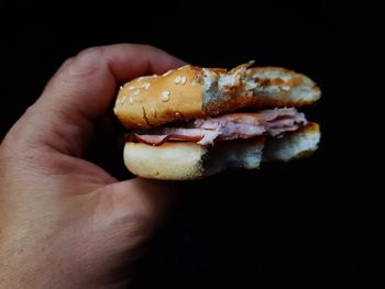 Close-up of hand holding hot dog against black background