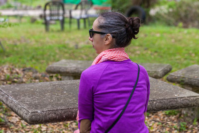 Rear view of mid adult woman wearing sunglasses sitting at park