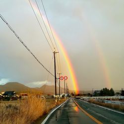 Rainbow over road against sky during sunset