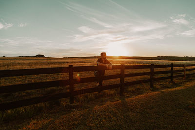 Man sitting on field against sky
