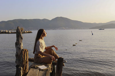 Woman sitting on handmade fishing platform in front of sea