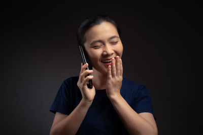 Smiling young woman using smart phone against black background