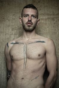 Portrait of shirtless man standing against wall