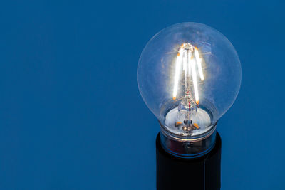 Low angle view of illuminated light bulb against blue sky
